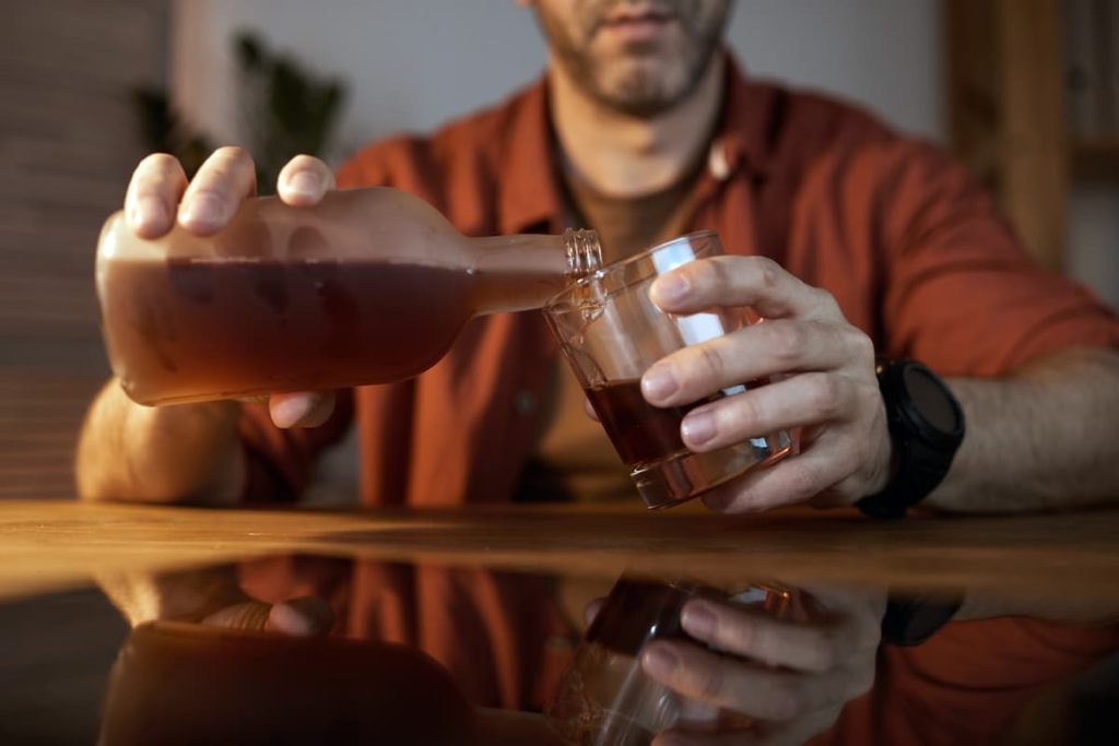 A man struggling with an alcohol addiction pouring a drink.
