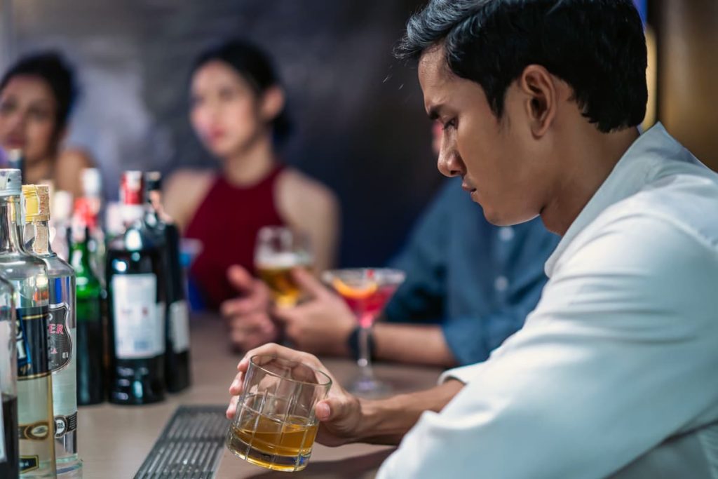 A young man struggling with substance abuse at a crowded bar.